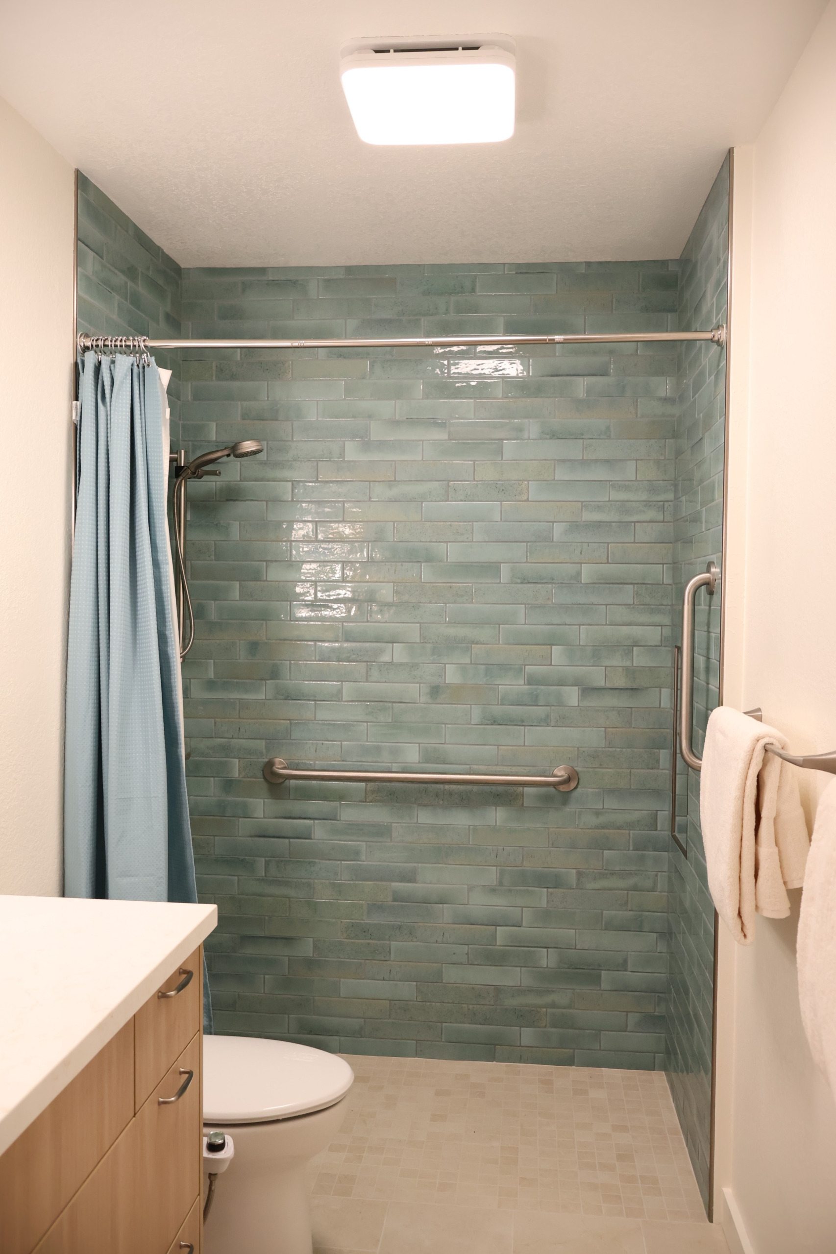 Curbless walk-in shower featuring Daltile Vitality tile, grab bars, and a calming sea-and-sand inspired color palette.